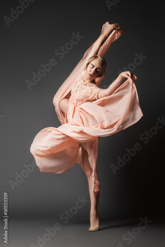 Woman in light chiffon dress dancing sensually on black plain background.