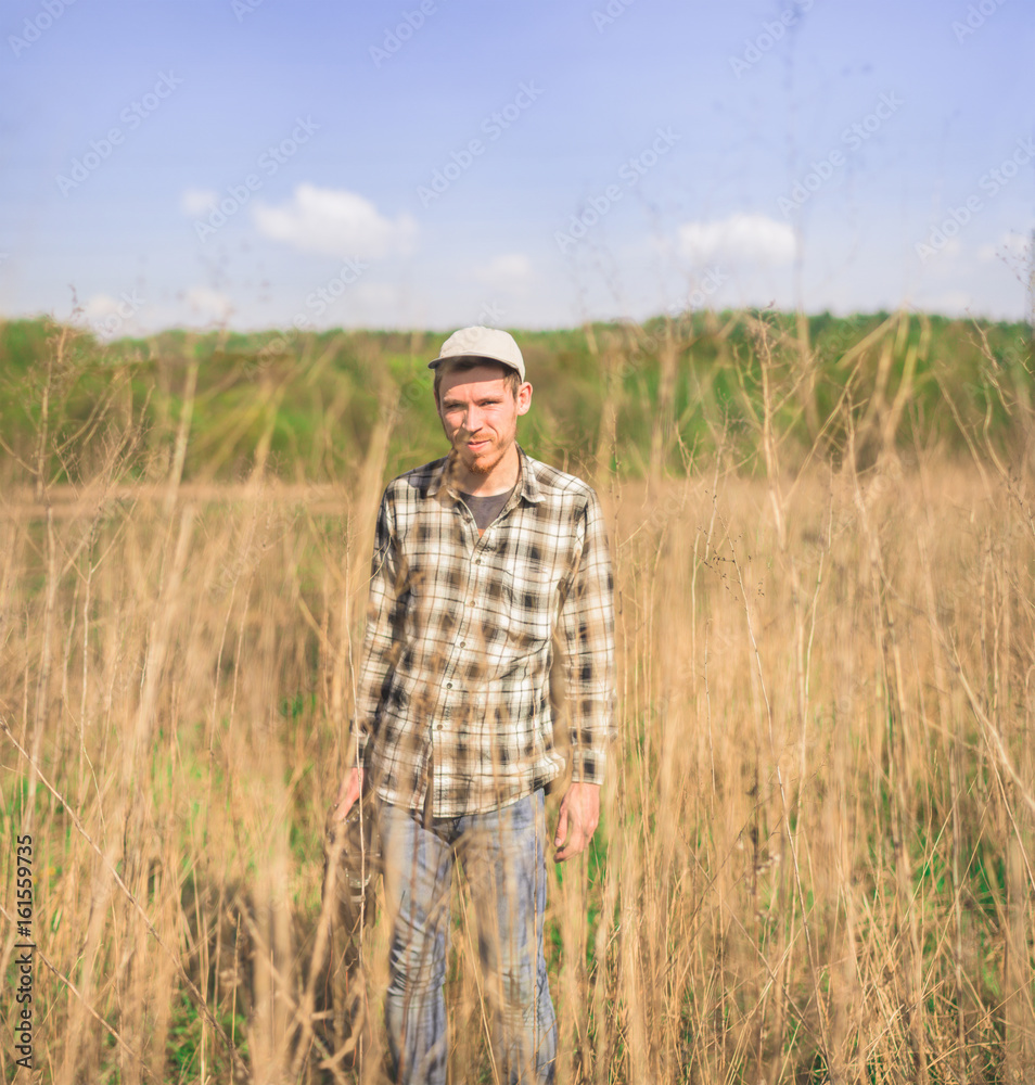 A hipster man in a plaid shirt stands in a dry tall grass