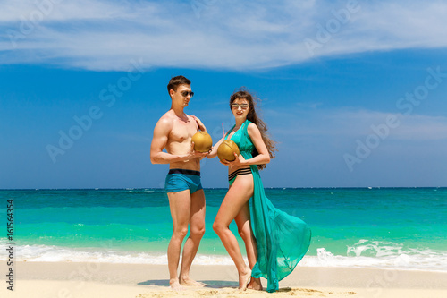 Young loving couple drink coconut on tropical beach. Summer vacation concept.