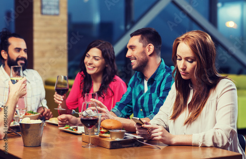 woman with smartphone and friends at restaurant