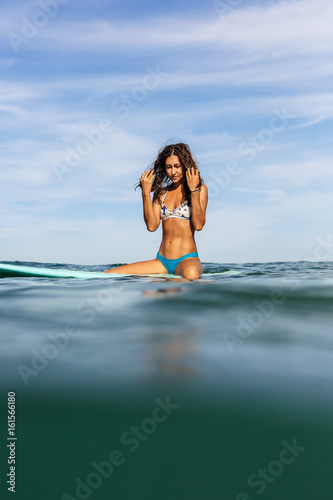 Photography Beautiful sporty surfing girl in sexy bikini sit on big longboard surf surfboard board on sunrise or sunset in the ocean and correct her hair