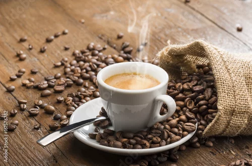Obraz steaming cup of coffee with burlap sack and coffee beans on wooden table.