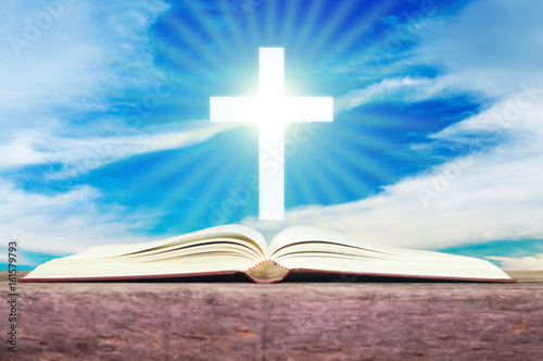 Open holy bible with white cross in the blue sky back ground.