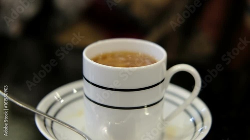 woman's hand holding little jar pouring milk in hot tea on table and stirring it. photo