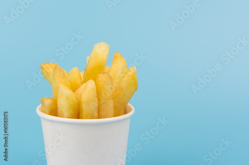 close up of french fries in a paper cup on blue background