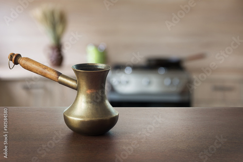 Vintage copper cezve with black coffee on wooden tabletop and defocused modern kitchen as background for display or montage your coffee products.