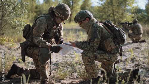 Obraz na plátně Two soldiers sitting in nature and using map and gps tracker for navigation