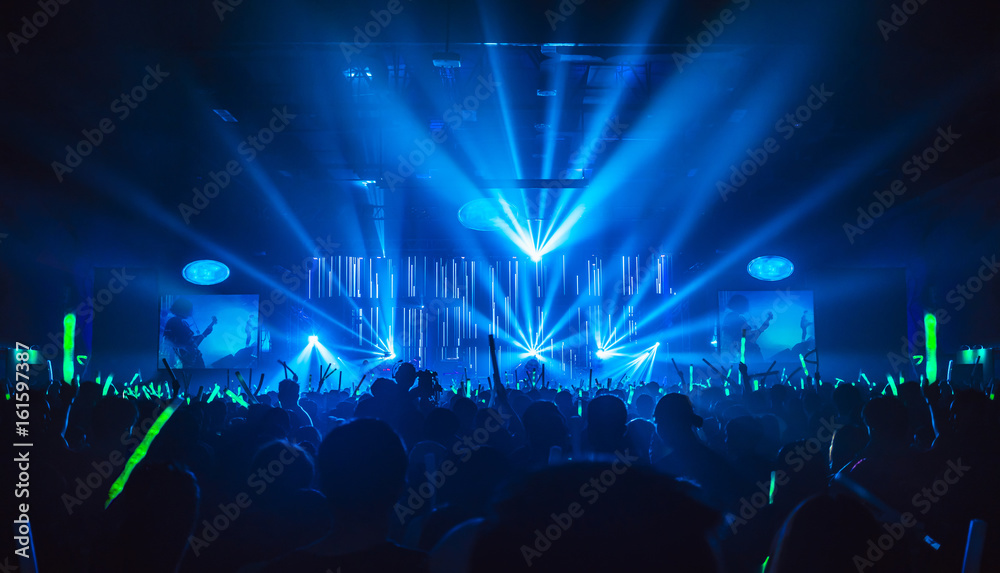 Silhouette in night club under blue rays beam and young people holding light saber enjoying at concert concept.