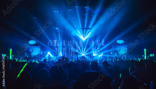 Fotografia Silhouette in night club under blue rays beam and young people holding light saber enjoying at concert concept