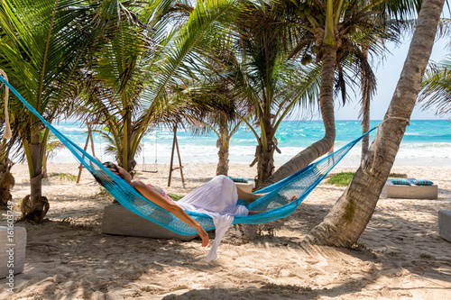 Junge Frau liegt in einer Hängematte unter Palmen am Strand der Karibik