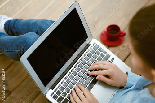 Woman sitting on the wooden textured floor and working with laptop in social networks. photo