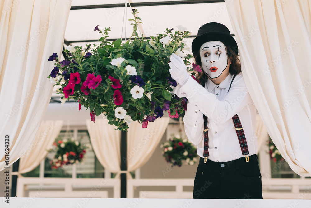Pantomime theater artist posing near the pot of summer flowers. - obrazy, fototapety, plakaty 