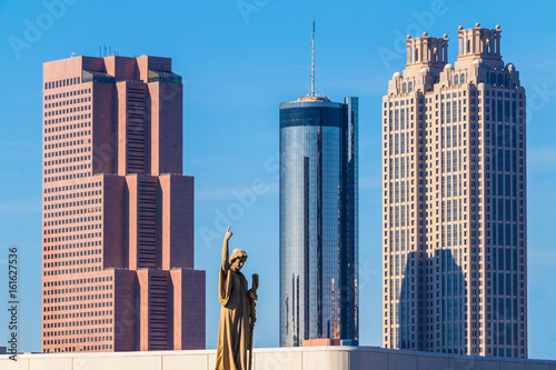 The sculpture of Virgin Mary on the Oakland Cemetery on the background of skyscrapers of Downtown in sunny day, Atlanta, USA