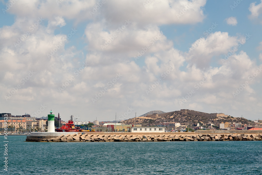 Cartagena, Spain - July 13, 2016: Green and white lighthouse, long breakwater at the entrance to the port.