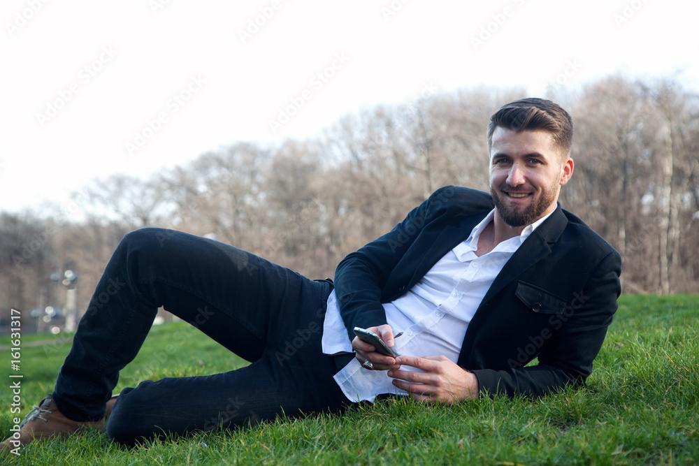 Geschäftsmann mit Smartphone ruht sich liegend auf einer Wiese im Park aus Geschäftsmann mit Smartphone ruht sich liegend auf einer Wiese im Park aus