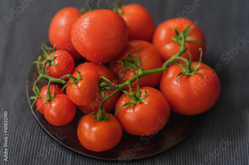 Bunch of Fresh red ripe tomatoes with branches with water drops, wooden plate, black background. Selective focus. Top view. Concept of vegetarian, healthy food