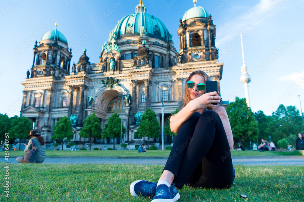 Fototapeta premium Pretty gil sitting in front of Berlin Cathedral doing selfie