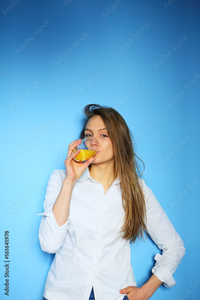 Woman drinking orange juice on a blue background in a white shirt Woman drinking orange juice on a blue background in a white shirt