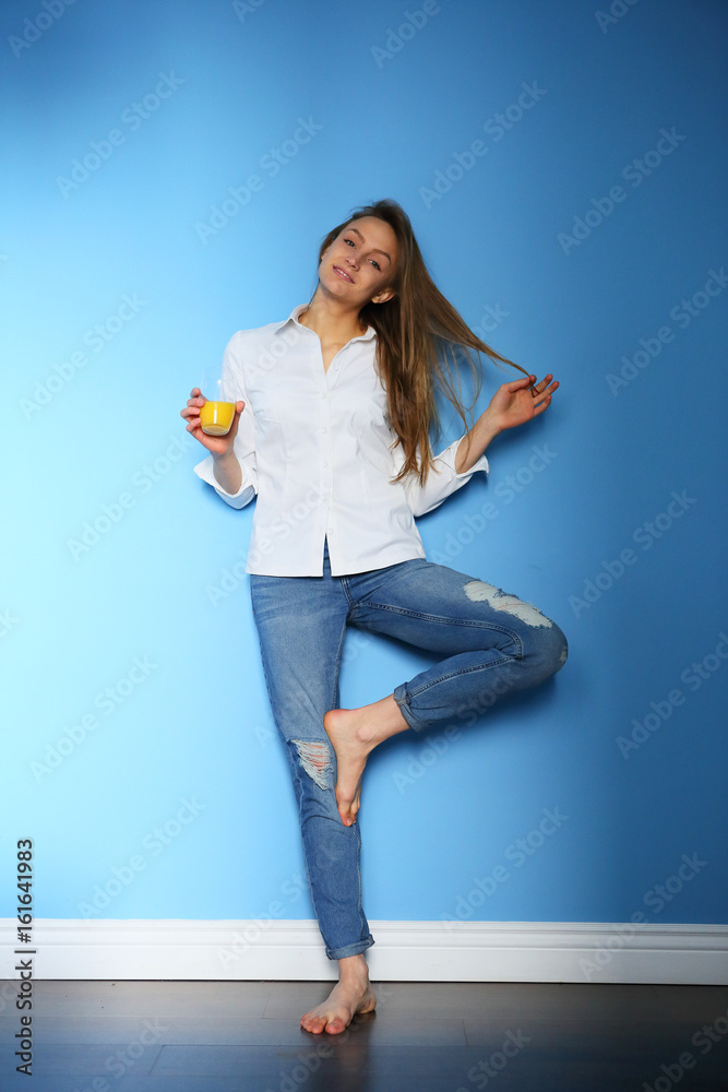 Smiling girl holding orange juice on a blue background with a white shirt and jeans Smiling girl holding orange juice on a blue background with a white shirt and jeans