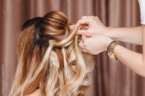Beautiful blonde girl with long hair doing an professional evening hairdress in a beauty salon