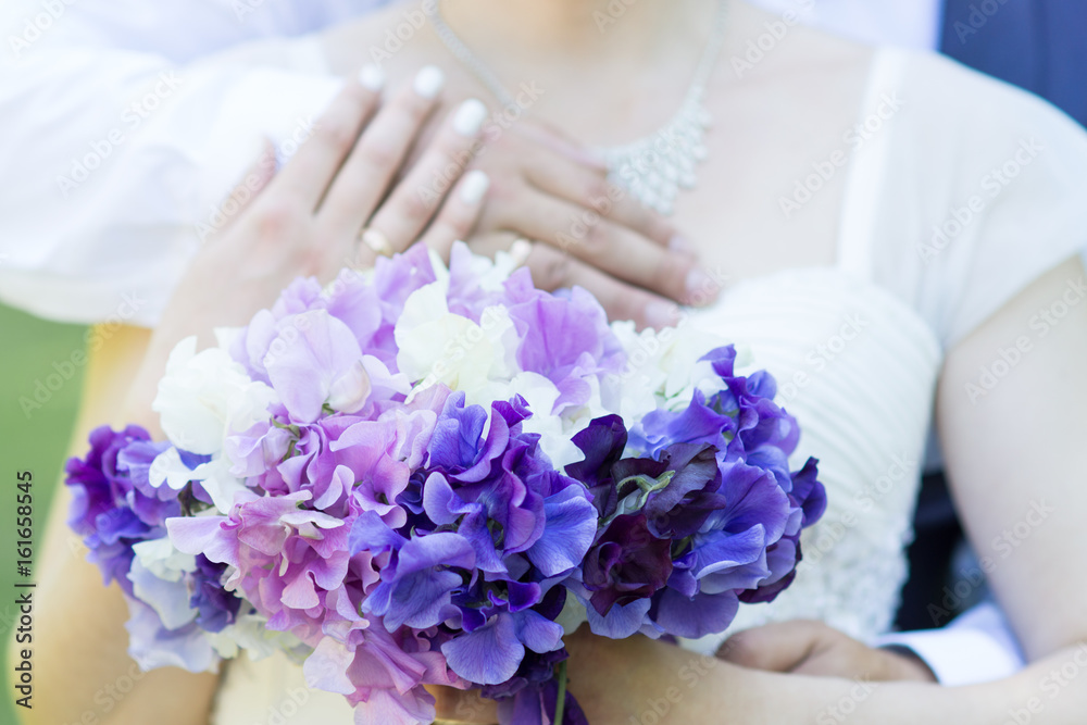 Hands of just married couple with golden wedding rings and sweet pea flowers at the background Hands of just married couple with golden wedding rings and sweet pea flowers at the background