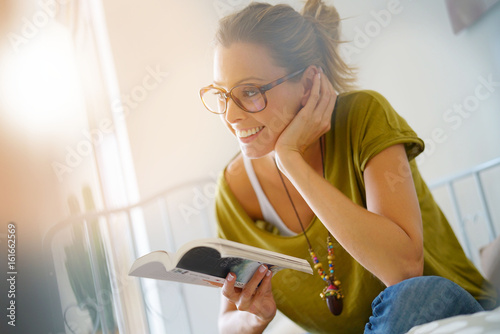 Tableau sur toile Trendy girl relaxing in sofa and reading book