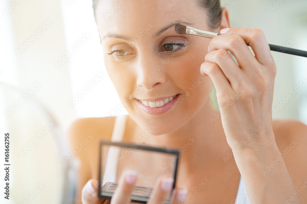 Young woman applying eyeshadow on - obrazy, fototapety, plakaty 