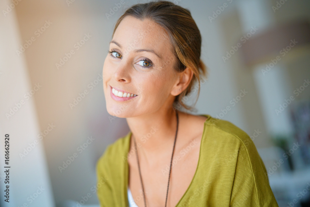 Cheerful woman standing in living-room with arms crossed