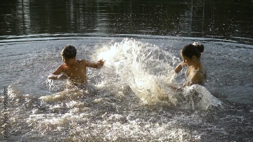 silhouette of two kids splashing water in pond at sunset