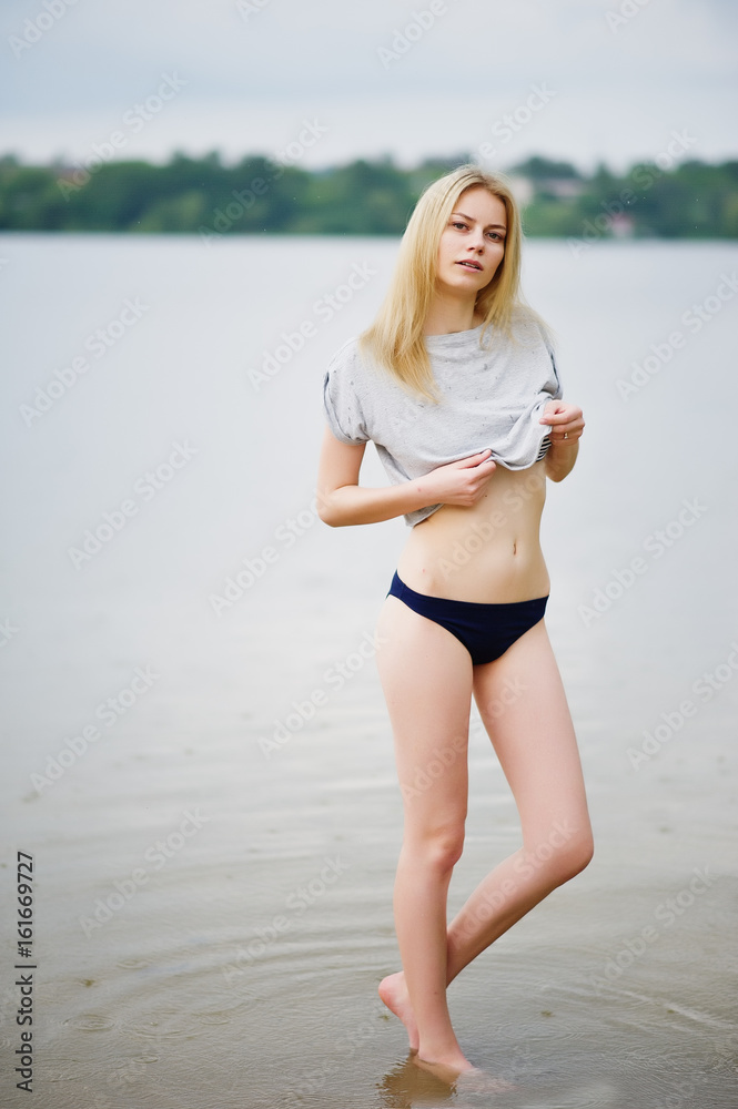 Portrait of a fantastically looking tall model wearing t-shirt and bikini walking in lake.