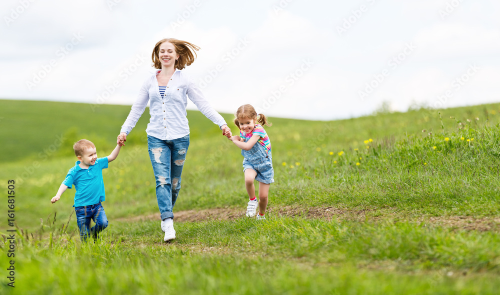 Happy family mother and children daughter and son laughing and running on   meadow in summer