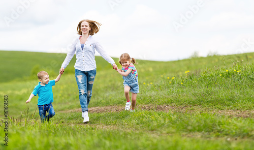 Happy family mother and children daughter and son laughing and running on meadow in summer