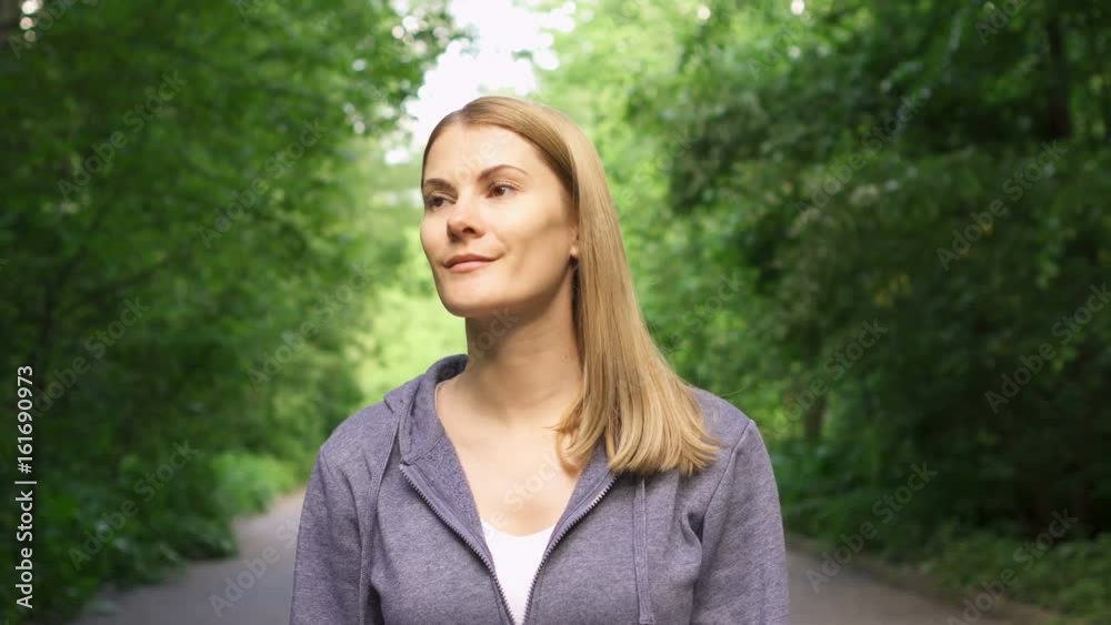 Slow Motion Happy smiling young woman in hoodies walking around in sunny park on summer's day Slow Motion Happy smiling young woman in hoodies walking around in sunny park on summer's day