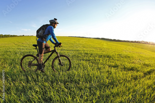 Fototapeta Naklejka Na Ścianę i Meble -  cyclist rides a bicycle on the green field towards the sun