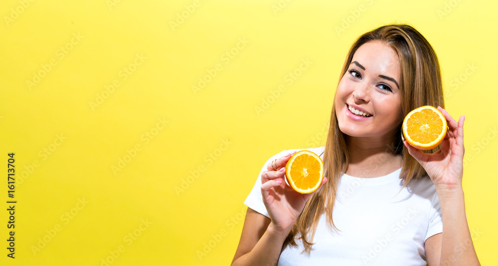 Happy young woman holding oranges halves on a yellow background Happy young woman holding oranges halves on a yellow background