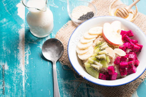 Bowl of oatmeal porridge with bananas, apple, dragon fruit and almonds. Top view photo