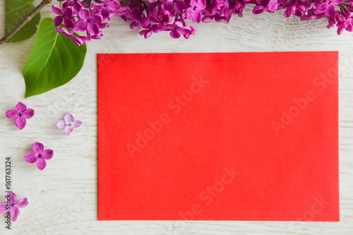 Purple lilac flowers with red blank greeting card on the wooden table.