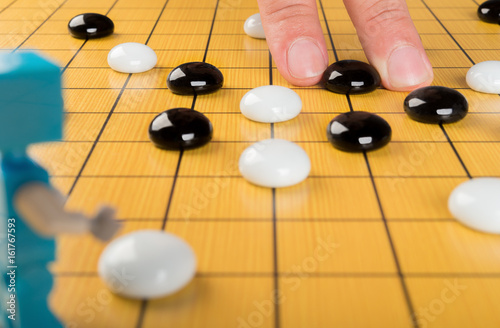fingers placing piece of GO on board with a robot in front  concept of human against robot