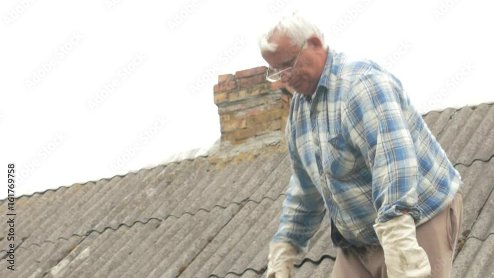 An elderly man is fixing the roof himself. Old wooden house in slate