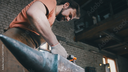 Blacksmith bends metal knife with gripe in workshop forge, portrait