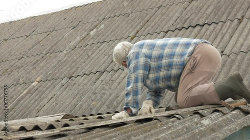 An elderly man is fixing the roof himself. Old wooden house in slate photo