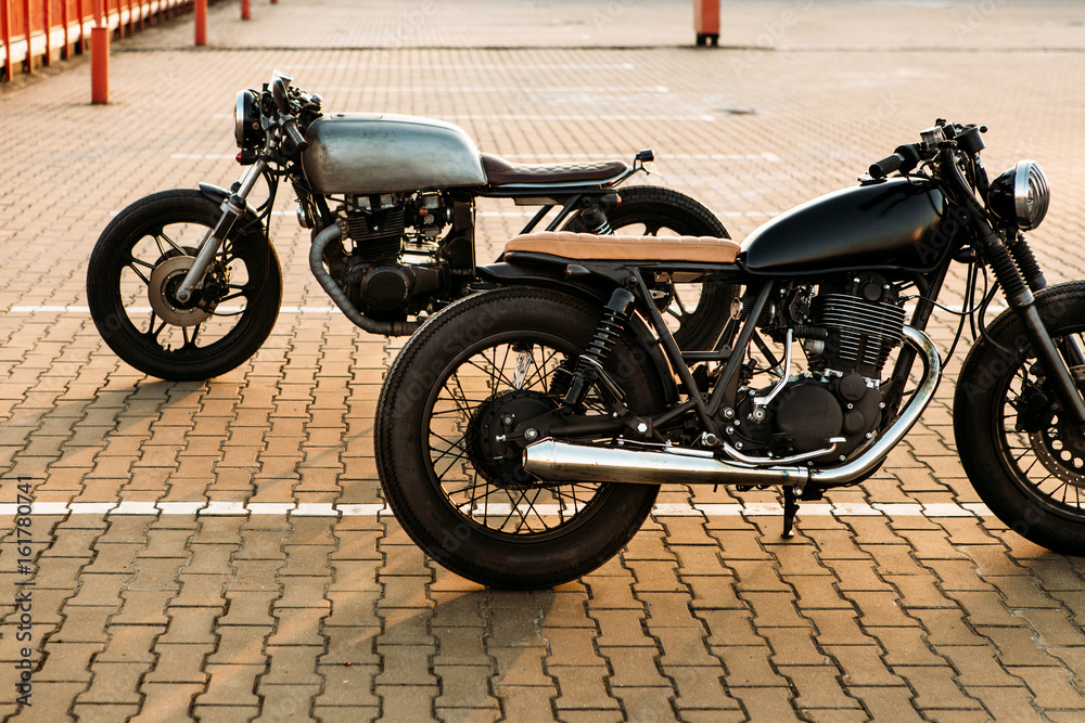Two brutal vintage custom motorcycle cafe racer looking in opposite directions on empty rooftop parking lot with during sunset. Symbol of wild ride, straight road, urban style, hipster lifestyle.