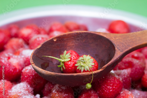 Against a background of strawberries with sugar a wooden spoon for jam. photo