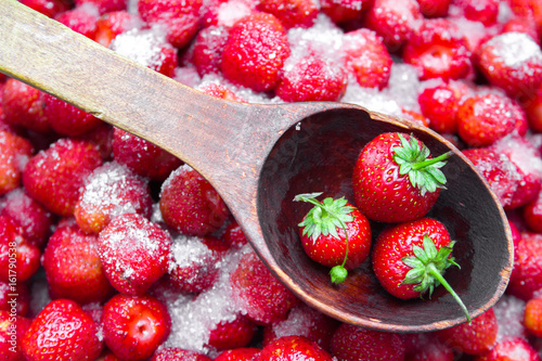 Against a background of strawberries with sugar a wooden spoon for jam. photo