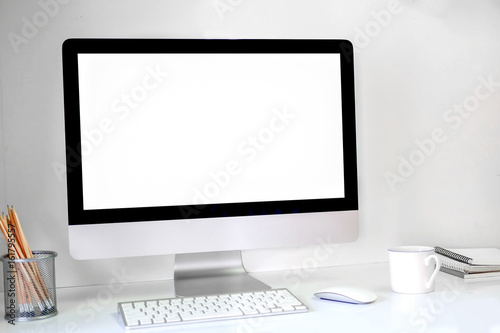 Creative hipster desktop with blank white computer screen, coffee cup and other items on white brick background. Mock up workspace.