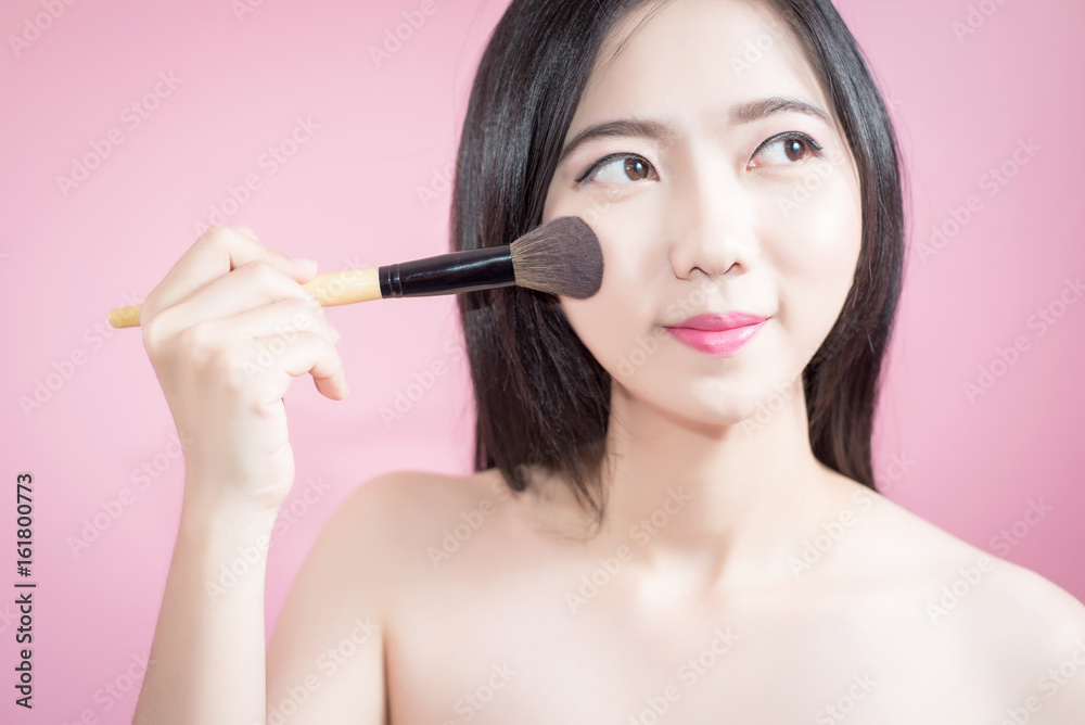 Long hair asian young beautiful woman applying cosmetic powder brush on smooth face isolated over pink background. natural makeup, SPA therapy, skincare, cosmetology and plastic surgery concept.