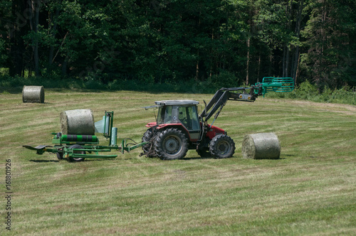 Tractor collecting a roll of haystack in the field