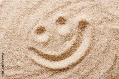 Happy smiling face in the sand. Eyes and mouth drawn with a finger in dry ocherous sand. Macro photo close up from above. photo