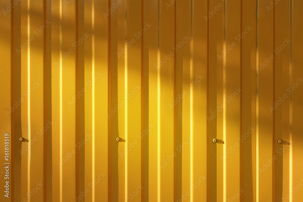 A corrugated fence of yellow metal sheets with screw. Texture of metal