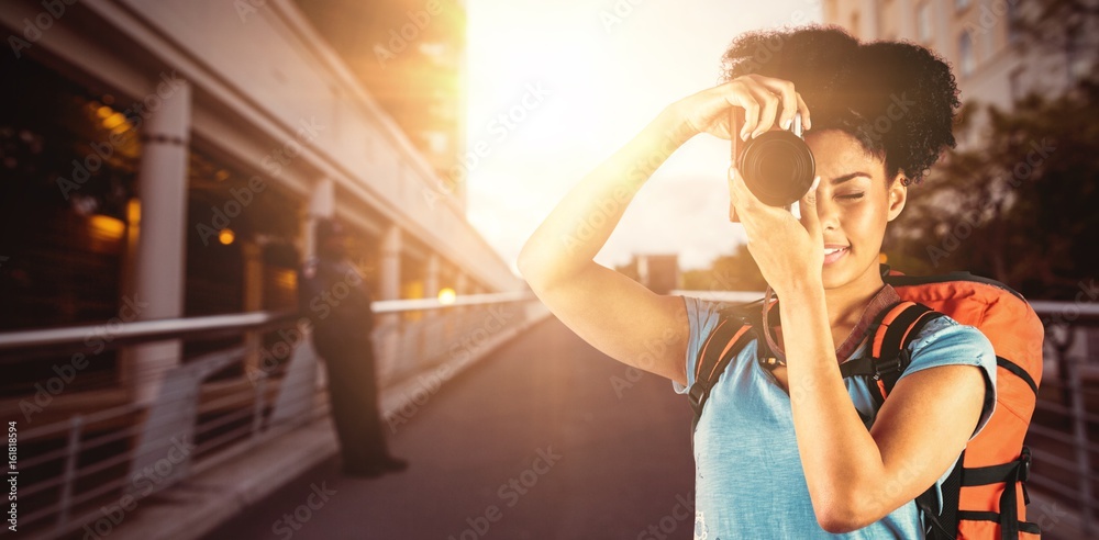 Composite image of young woman with backpack taking picture